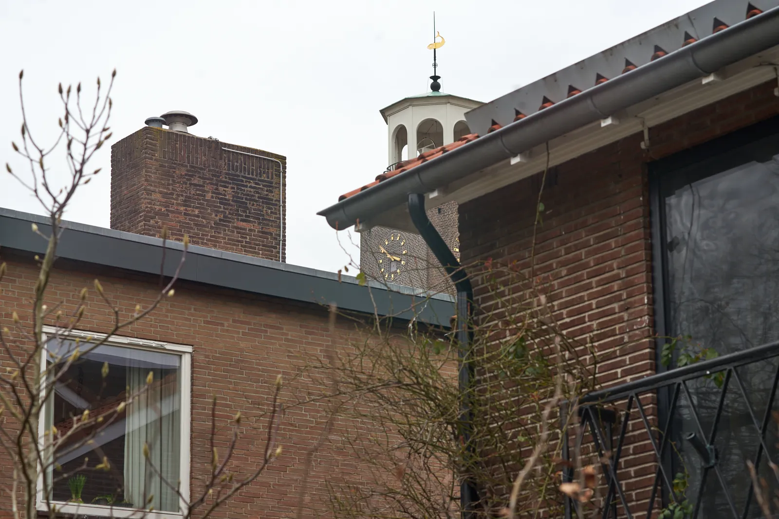 Between some houses, in the background there’s the clock on a chruch tower. It says it’s 15:51.