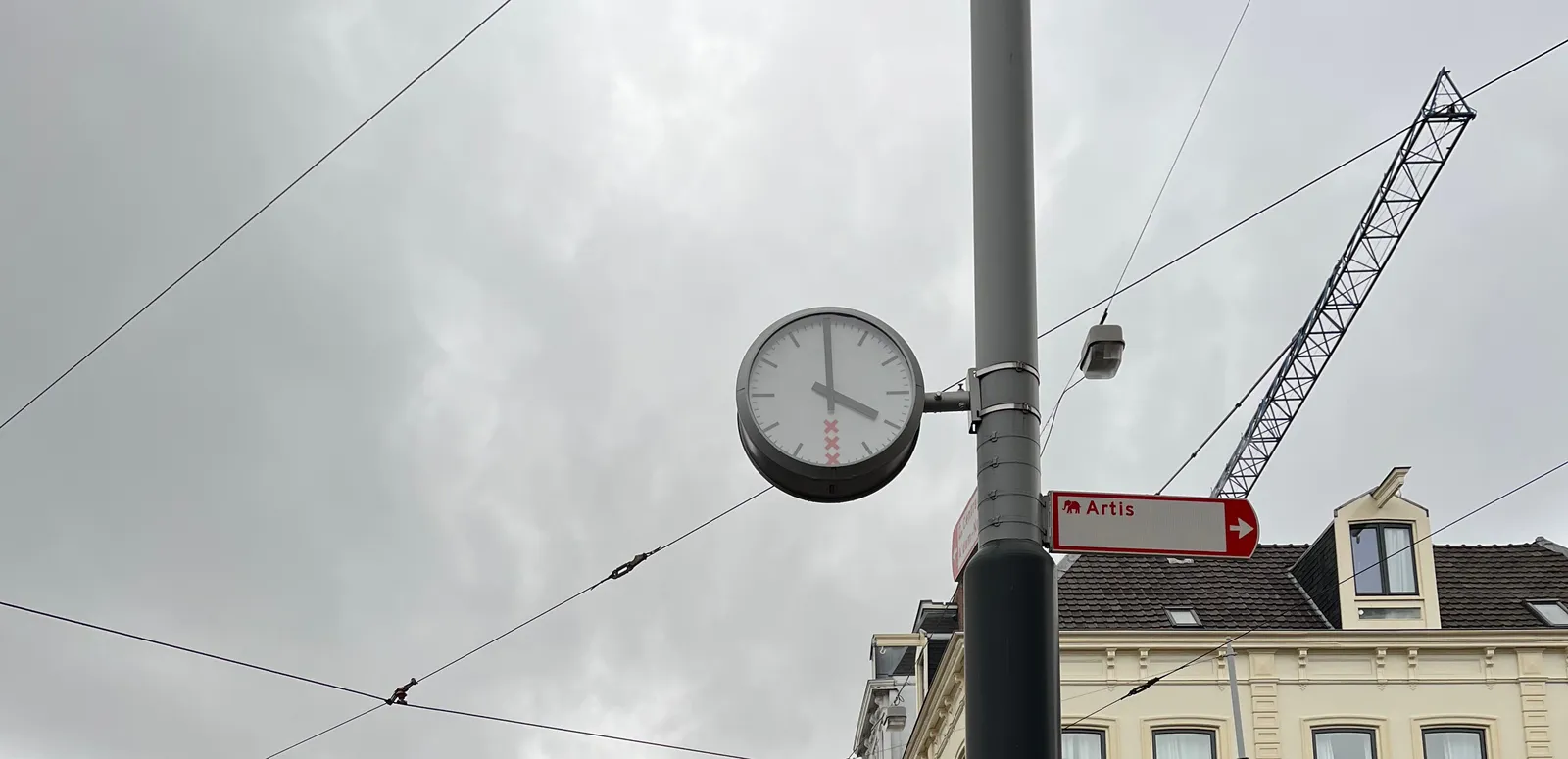Attached to this pole is a sign that points at Artis, the zoo in Amsterdam. There’s a clock attached to the same pole, which points at 4 o’clock. 