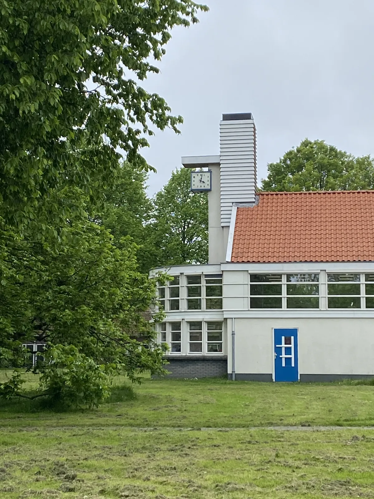 This clock, attached to a modernist building surrounded by trees points at 2 minutes past 4.