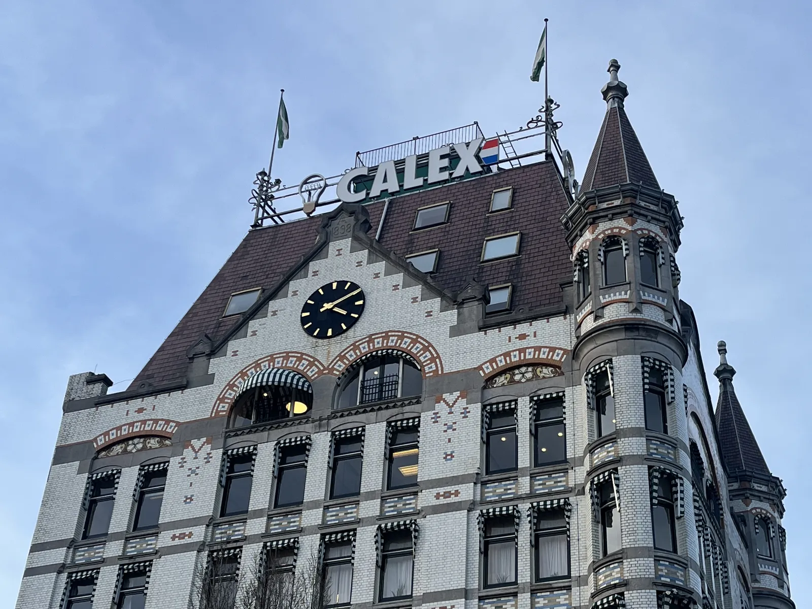 A closeup of the top floors of the famous white house in Rotterdam. There’s a clock on its facade which points at 10 past four.