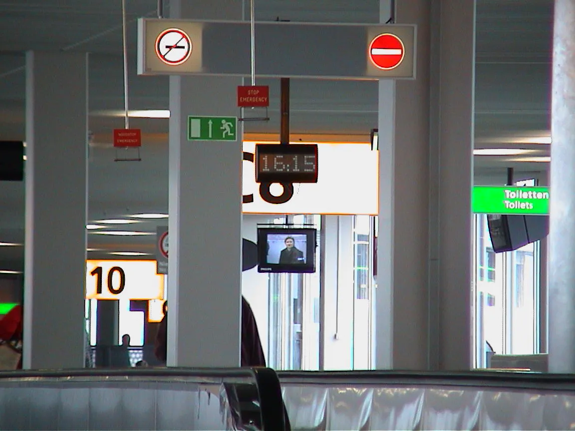 A clock in something that looks like an airport, says it is 16:15