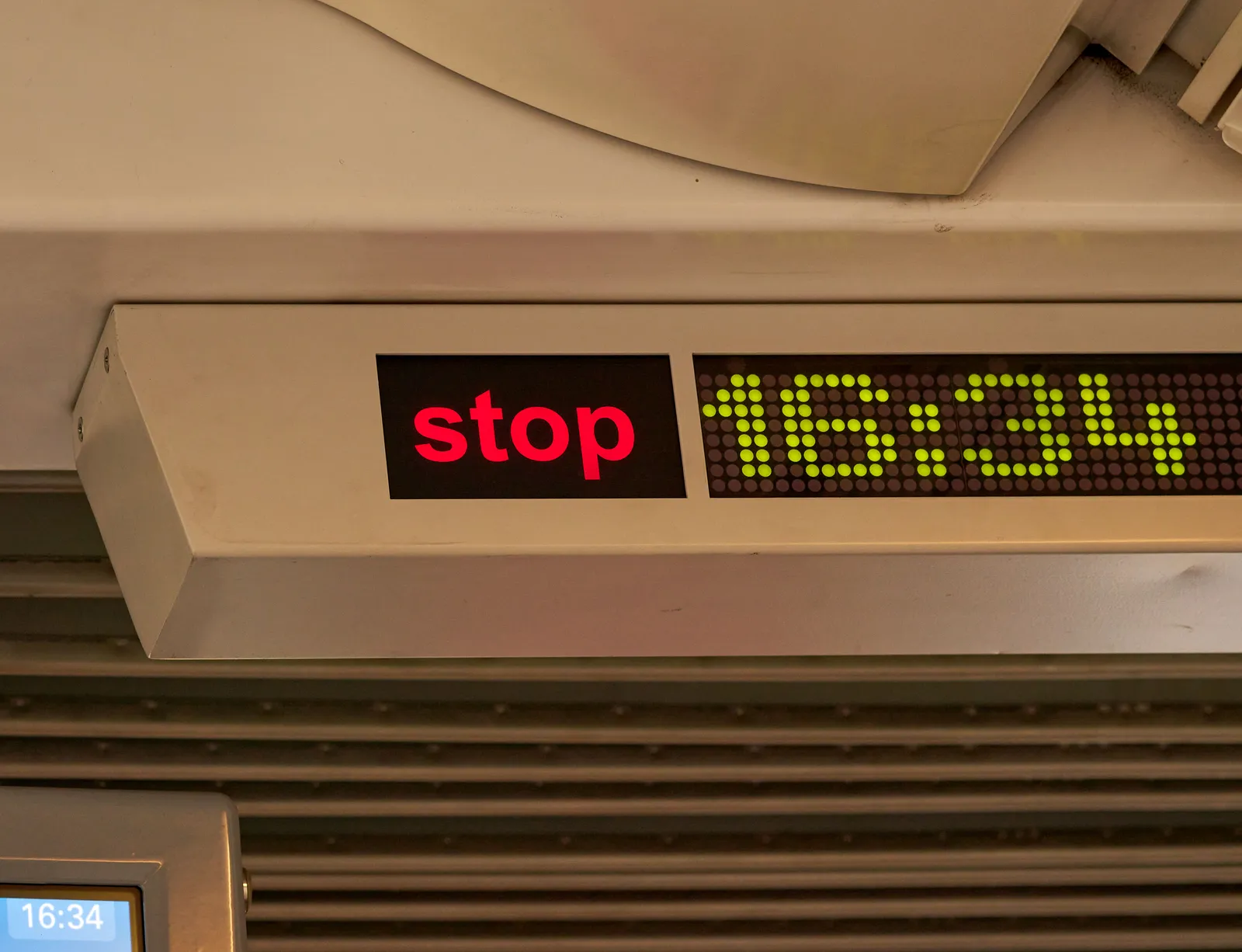 The stop sign is on, so the tram will soon open its doors. Next to the stop sign the time says it is 34 past four.