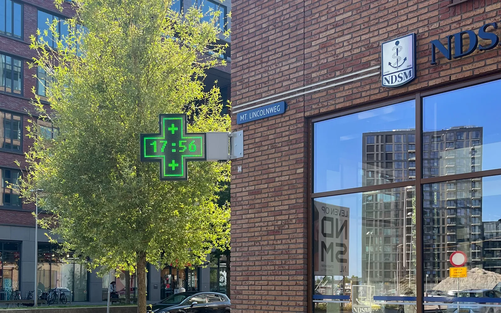 A digital cross shaped display, attached to a pharmacy. It says it is 17:56