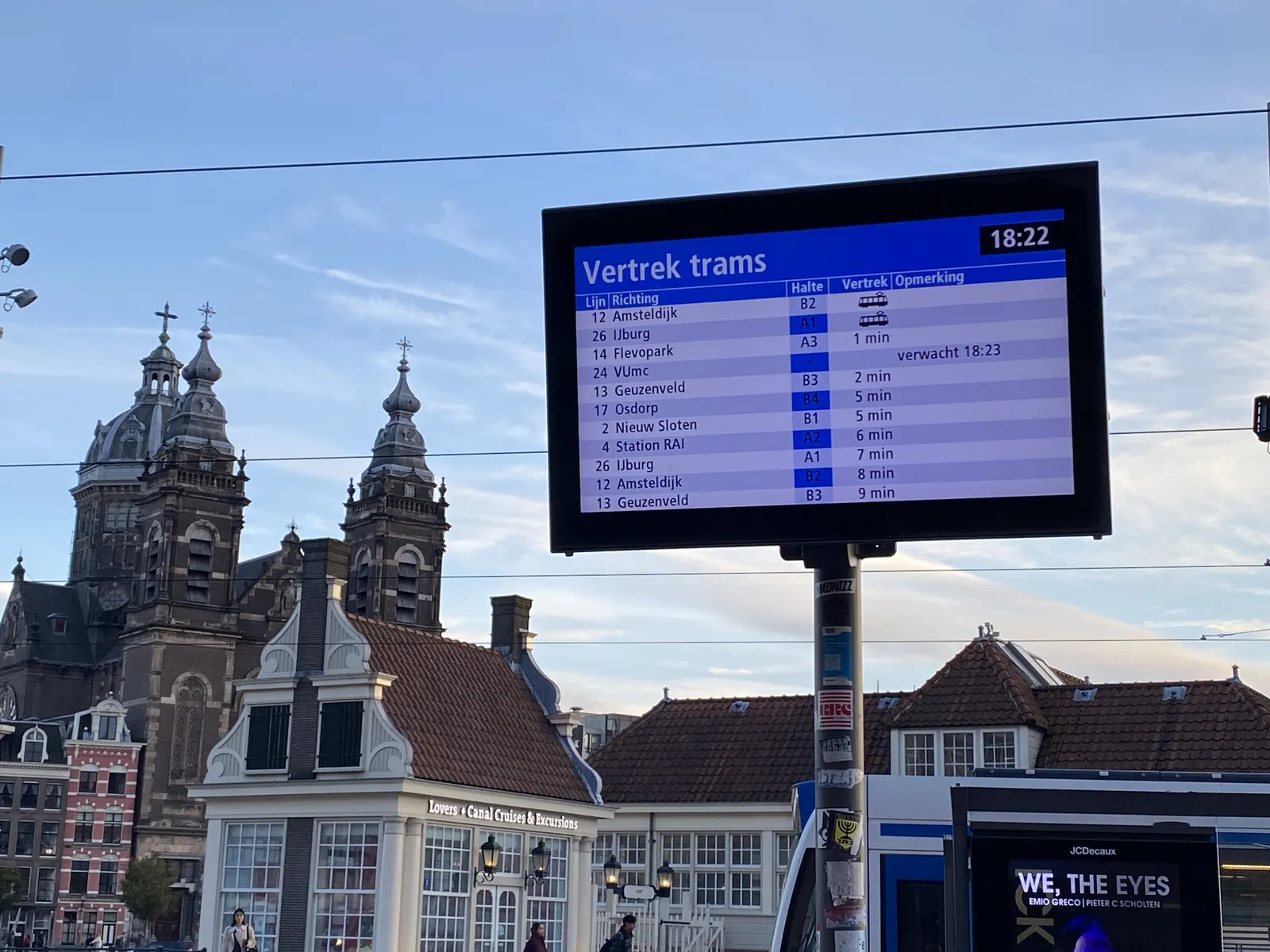 In the background a large old church and some other interesting looking buildings. In front, there’s a display, with a long list that shows in how many minutes the trams will depart. The time is shown as well. It is 18:22.
