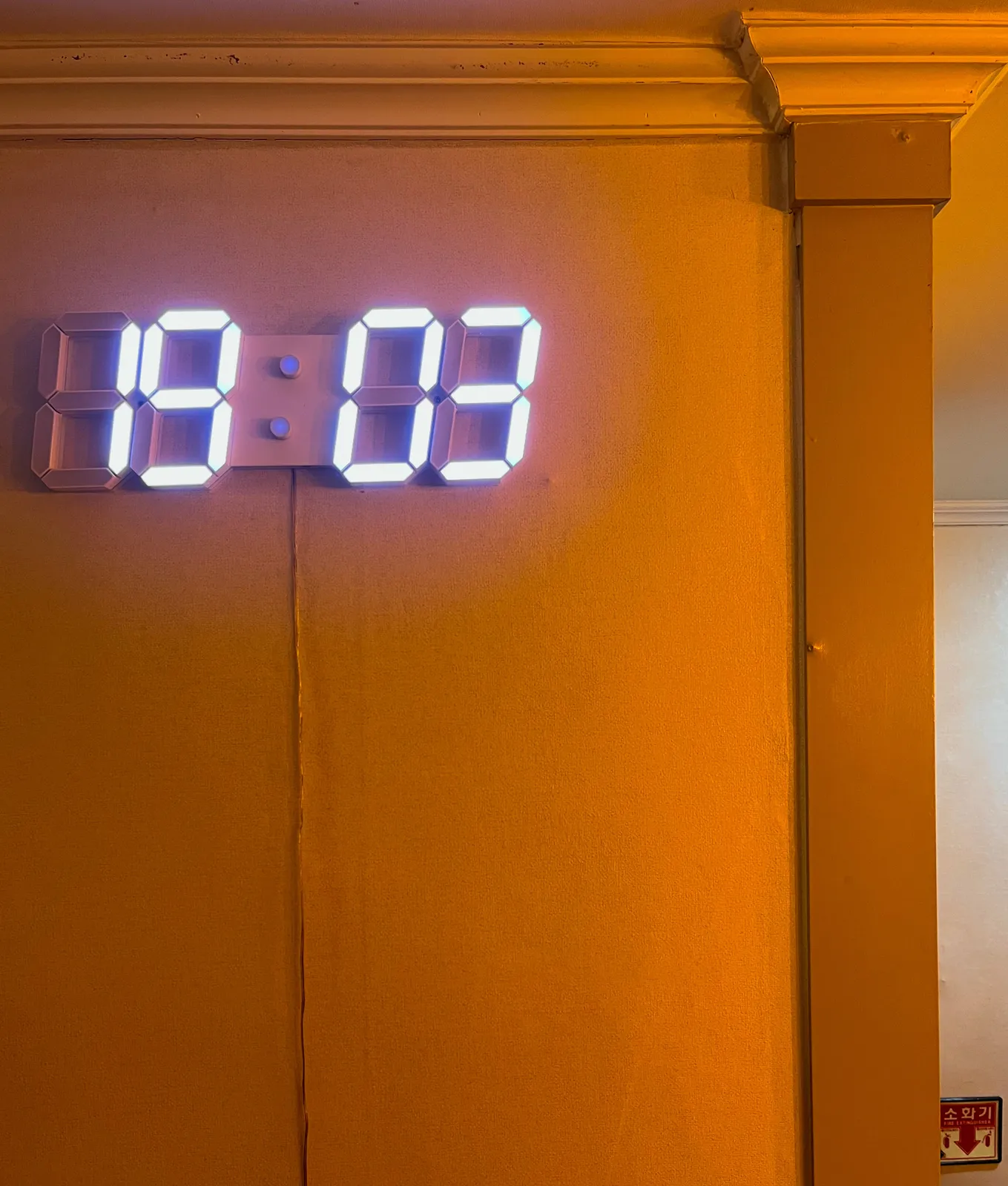 A segmented clock hanging on a yellow wall. It shows the time as 19:03