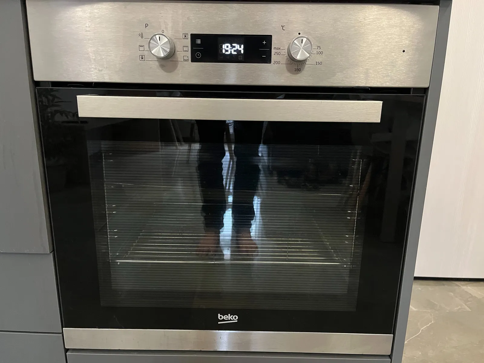 The feet of the photographer are mirrored in the glass of this oven’s door. On its digital display the time is shown as 19:24