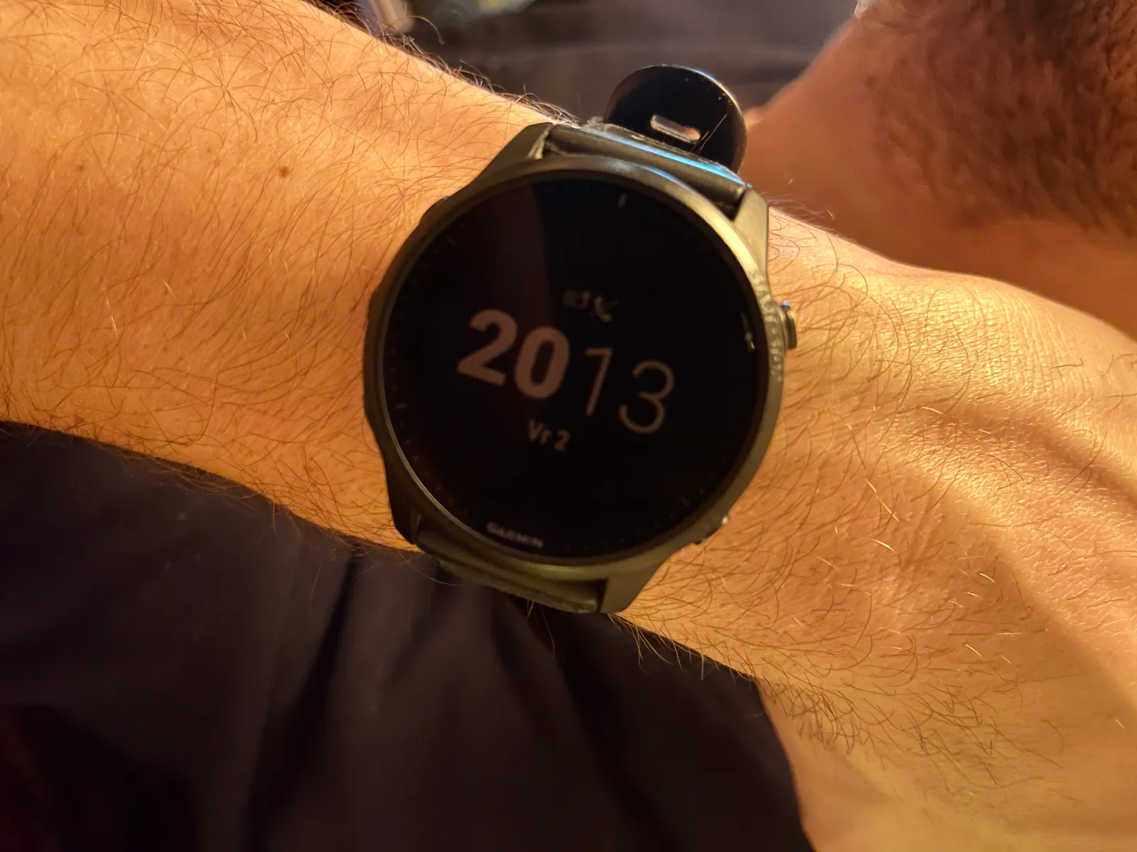 A dark wrist watch on someone’s wrist. It uses digits to display the time, but not the classic digital digits. It uses a more modern sans serif font. The digits that display the hour are printed bold, the minutes are thin. It shows the time as twenty thirteen.