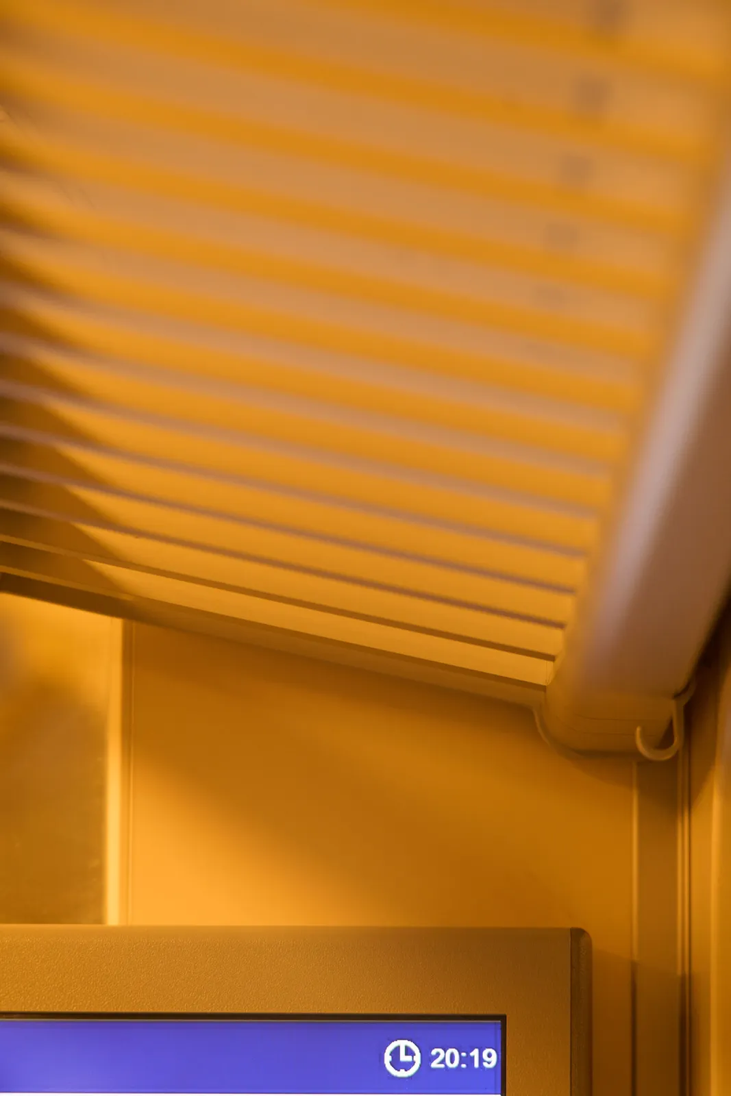 A rather abstract picture which turns out to be a luggage rack in a train with a digital display right underneath it. On the display the time is shown as 20:19