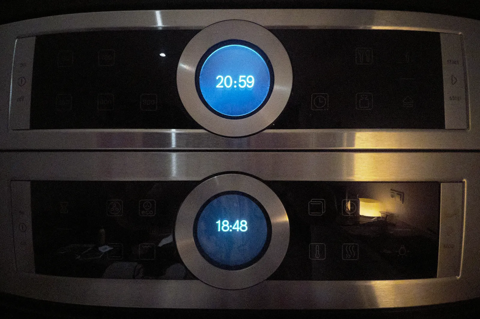 There are two identical digital clocks, one above the other, both part of the display of an oven. The clock on the bottom says the time is 18:48, the one on top says it is 20:59