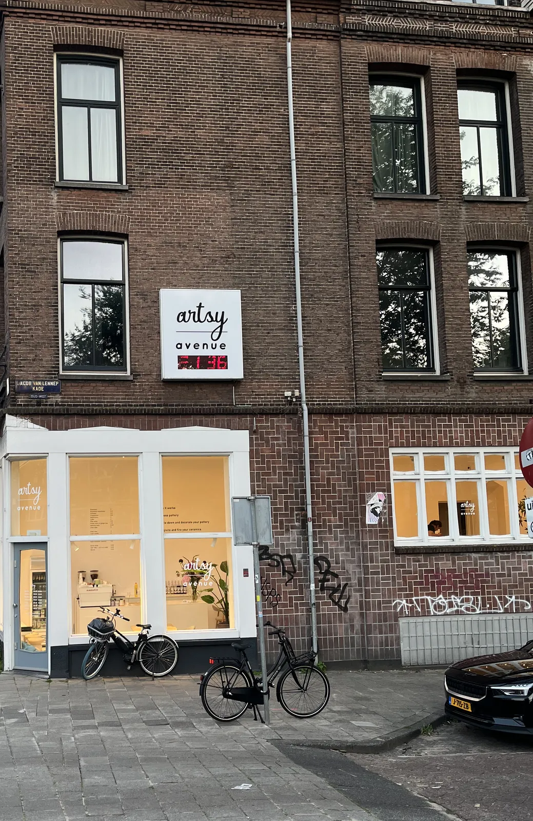 A brick facade with a digital clock attached to it. It says Artsy Avenue on this clock. And it displays the time as 21:36