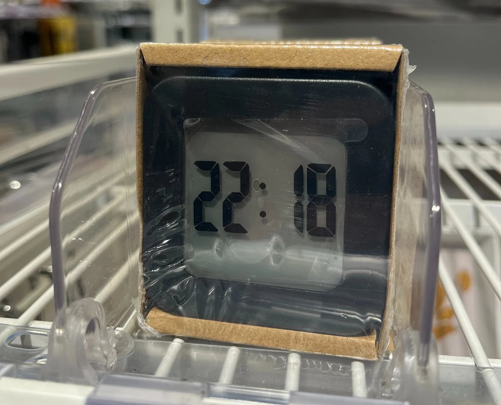 A digital clock is for sale. It’s wrapped in plastic. On the plastic a timestamp is printed. It says it is 22:18.