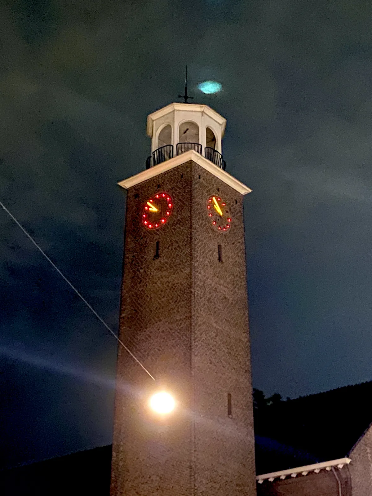 A church tower in the dark. It points at 8 minutes to 11.