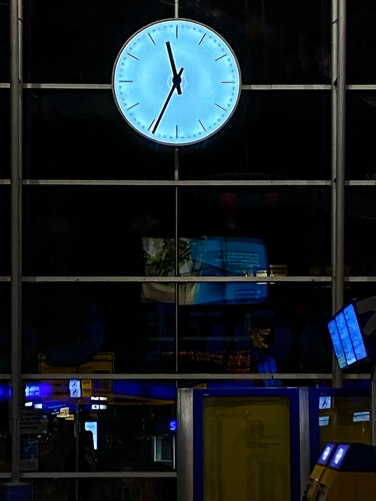 In a glass facade there’s a lit clock, standing out against the dark night sky. It points at 34 minutes past 11.