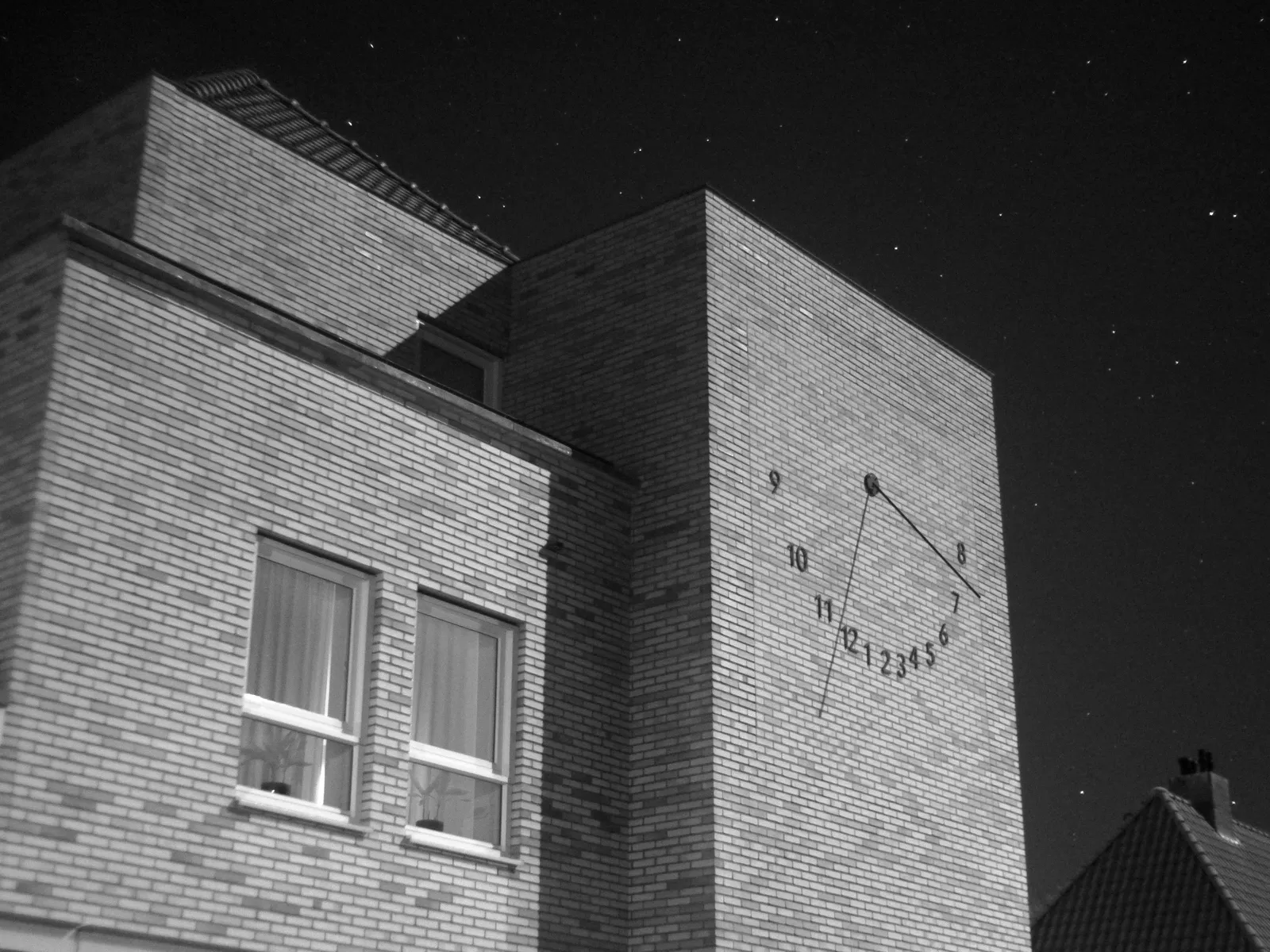 An infrared, black and white picture of a facade with a sun dial on it. It’s night but the moon casts a shadow at 40 past 11.