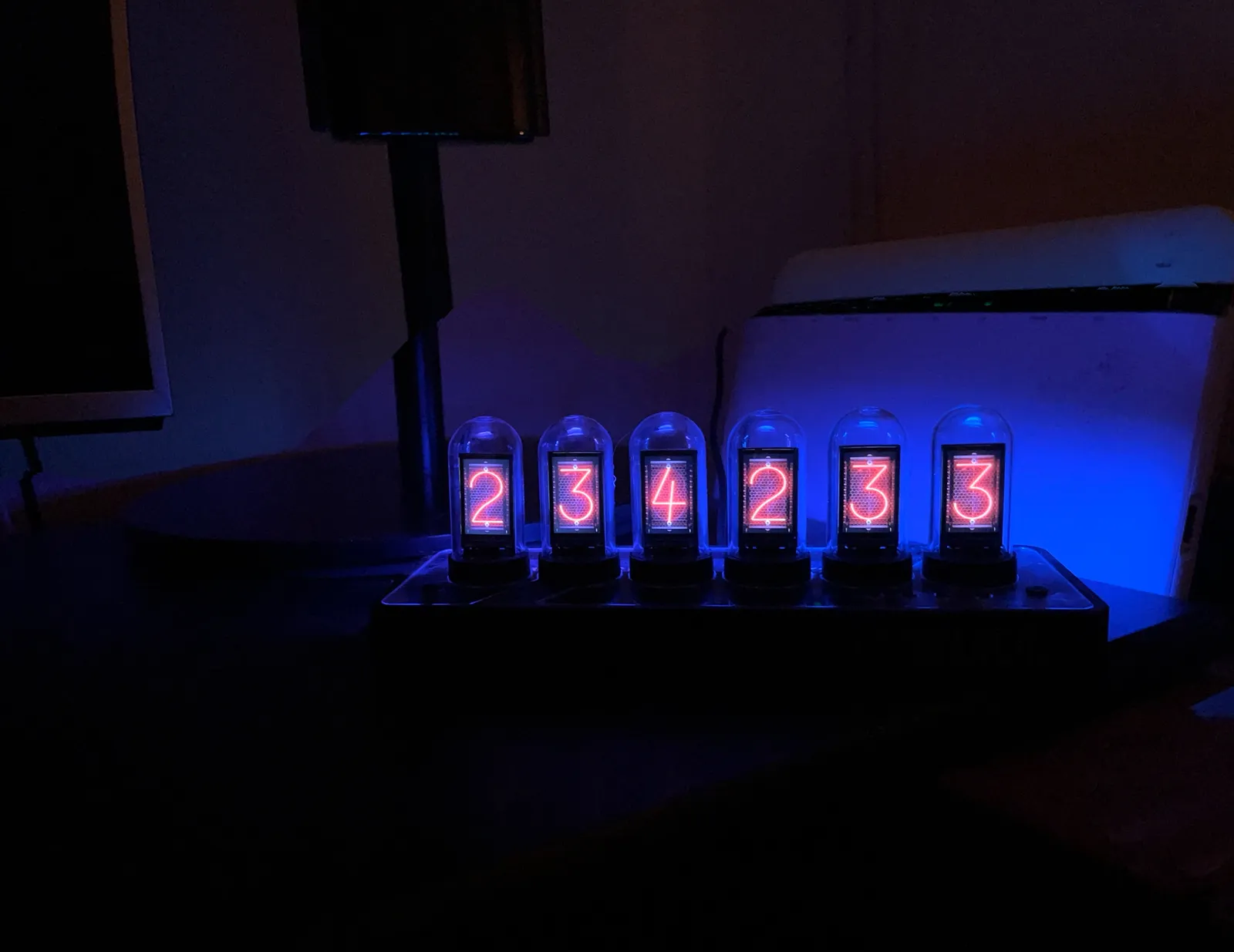 A clock made from vacuum tubes with glowing numbers in them. The dark surroundings are lit with a blue glow. The tubes say that it is 23:42. It even says 33 seconds, but that might be inaccurate right now.