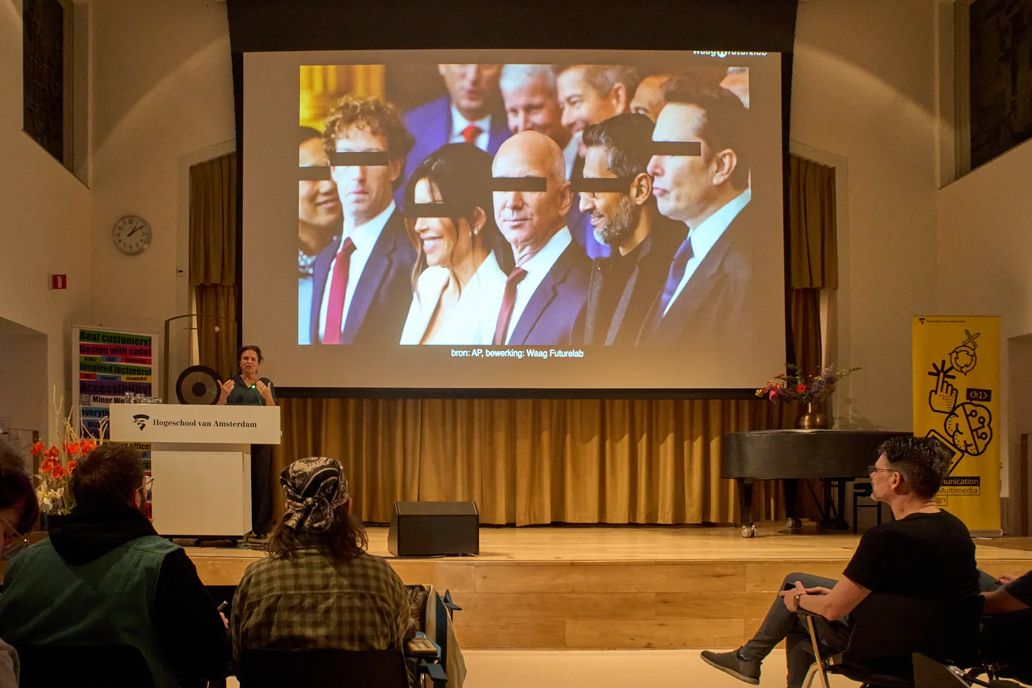 A group of billionares with black bars over their eyes shown on a big screen by someone behind a lectern