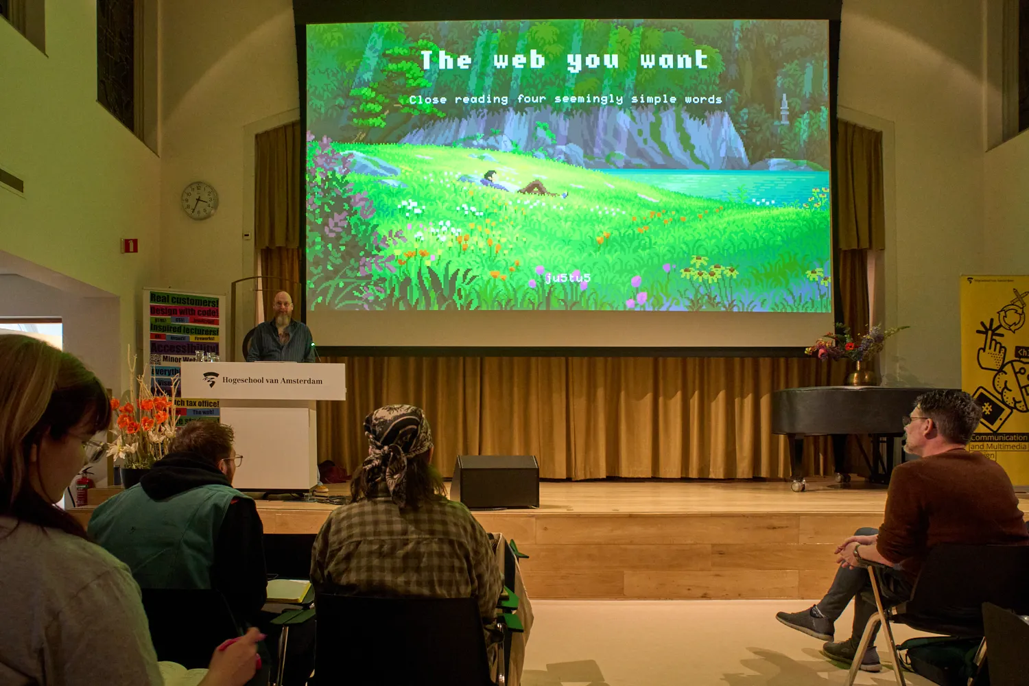 A pixelated, green landscape, shown on a big screen by someone behind a lectern